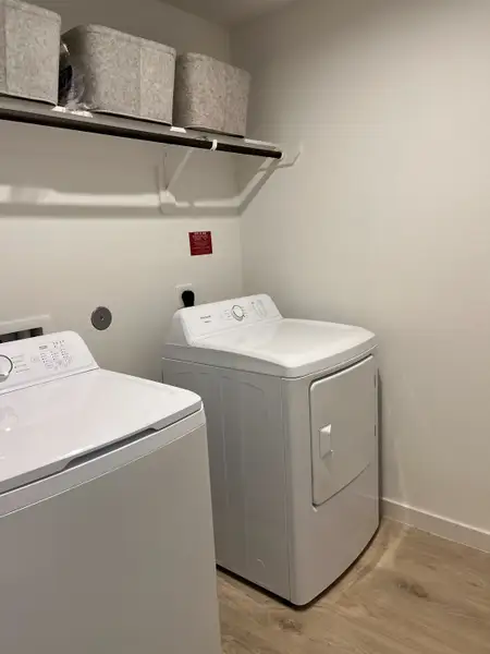 A functional laundry room with modern washer, dryer, and storage baskets on a shelf above.