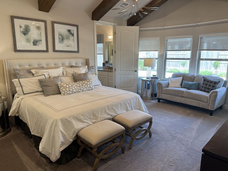 A spacious bedroom with elegant decor, featuring a plush bed, cozy seating, and abundant natural light from large windows.