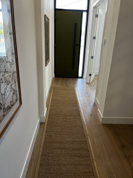 Stylish entryway with a textured runner rug, framed artwork, and a bold green door.