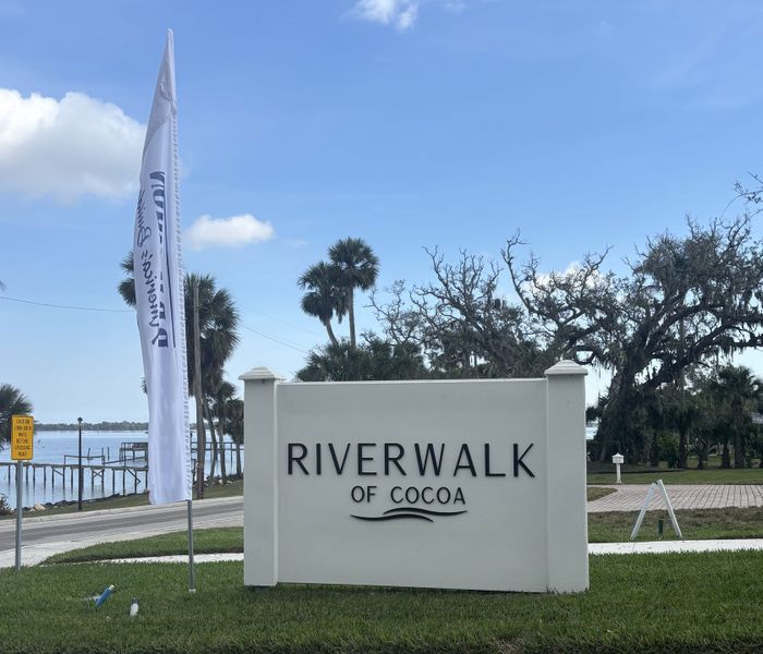 Entry sign for Riverwalk of Cocoa, with a scenic waterfront and lush greenery.