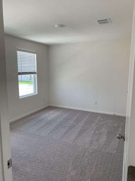 A bright, cozy room with soft grey carpet, neutral walls, and a sunlit window, perfect for relaxation or productivity.
