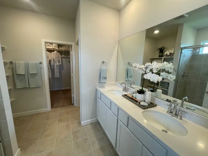 A modern bathroom with dual sinks, large mirror, and decorative orchid, leading to a spacious walk-in closet.