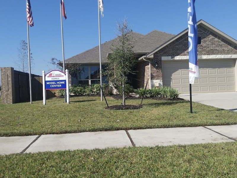 A well-manicured model home in Cobblestone by Adams Homes, featuring a classic brick façade and a spacious front yard.