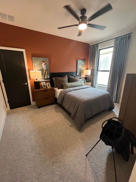 A cozy bedroom featuring a warm accent wall, modern ceiling fan, and elegant decor with framed art pieces.