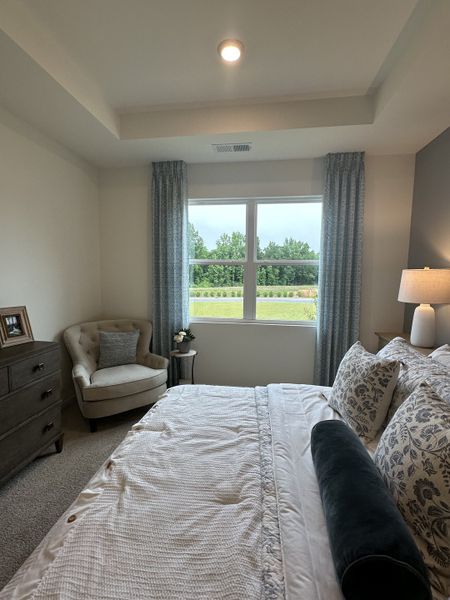 A cozy bedroom featuring elegant drapes, plush bedding, a soft armchair, and abundant natural light through the window.