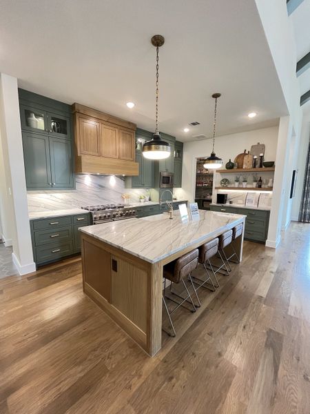 A modern kitchen with a marble island, sleek green cabinets, and pendant lighting, featuring hardwood floors.