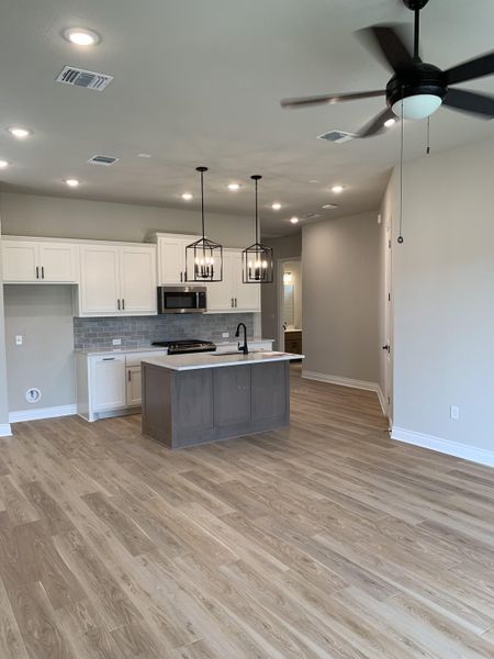 An elegant kitchen with sleek lighting, wood floors, and modern cabinetry.