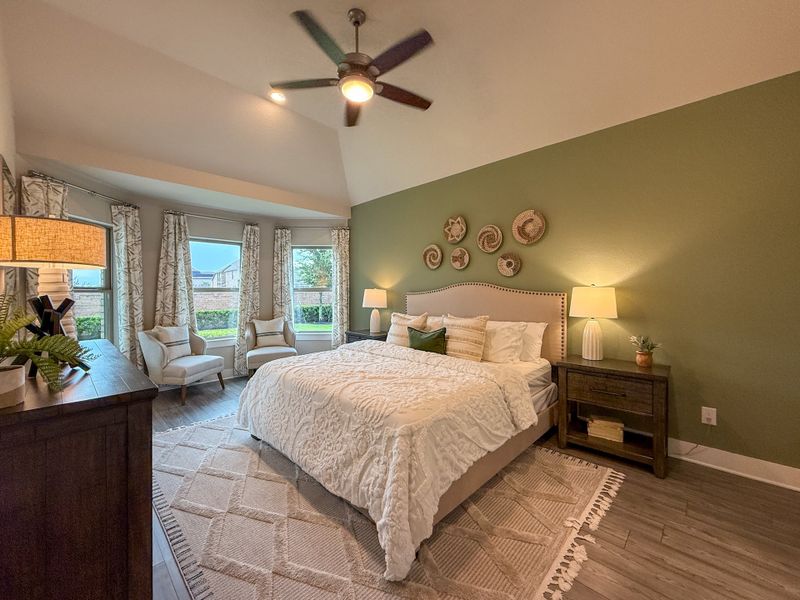 A cozy bedroom featuring sage green walls, a plush bed, and elegant decor with natural light streaming through large windows.