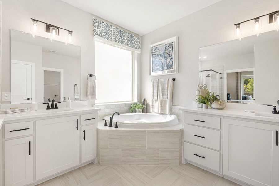 Master bathroom with dual vanities, white cabinets, and a corner soaking tub beneath a window