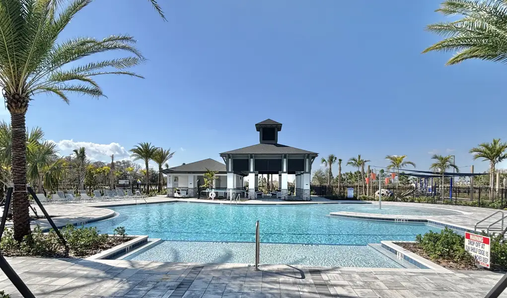 A resort-style pool with a covered pavilion, palm trees, and ample lounge seating in Eden at Crossprairie by M/I Homes (St. Cloud, FL).