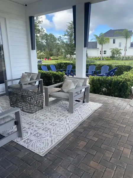 A cozy outdoor patio with modern seating, patterned rug, and lush garden views, perfect for relaxation.