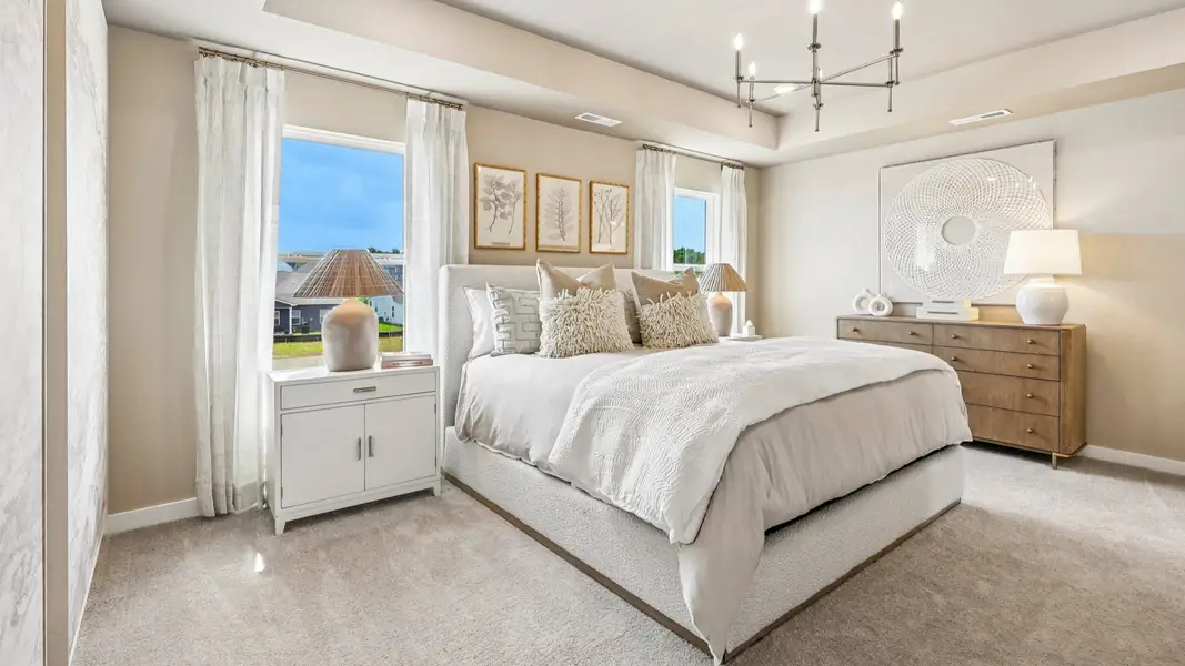 Primary suite with tray ceiling, windows, and carpet
