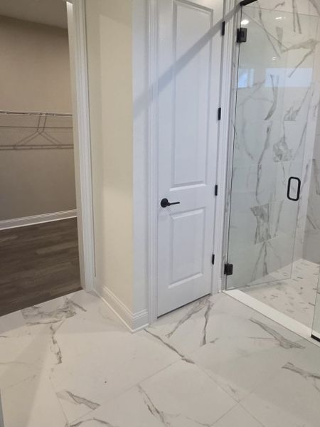 A sleek bathroom with marble-style tiles, a glass shower, and a walk-in closet.