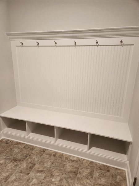 A sleek mudroom with bench seating, storage cubbies, and hooks, featuring a clean, modern design and tiled flooring.