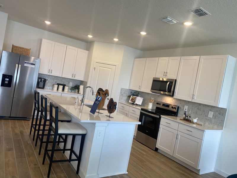 A modern kitchen with sleek white cabinetry, stainless steel appliances, and a spacious island with bar seating.