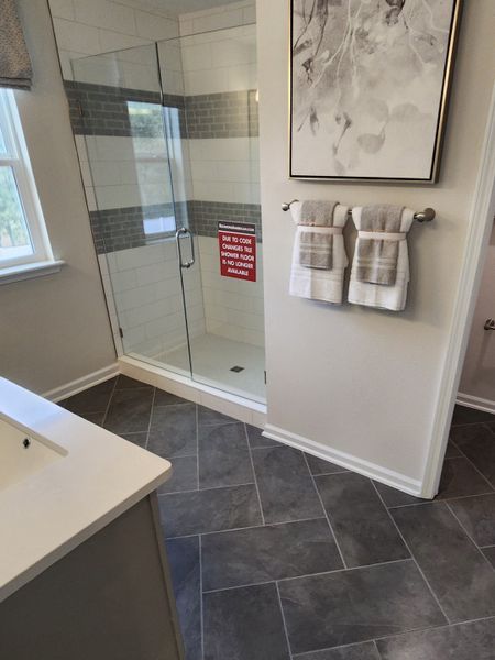 A modern bathroom with a spacious glass shower, elegant artwork, and plush towels over sleek tiled flooring.