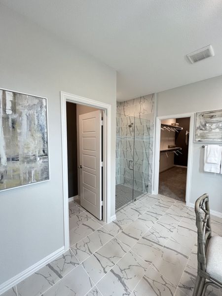 Elegant bathroom featuring marble-patterned tiles, glass shower, and modern art on the walls for a chic touch.