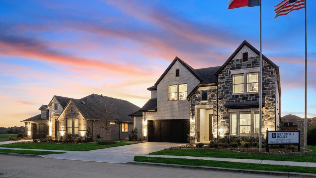 Bloomfield Homes model homes with stone and brick exteriors, two-car garage, and flagpoles at dusk