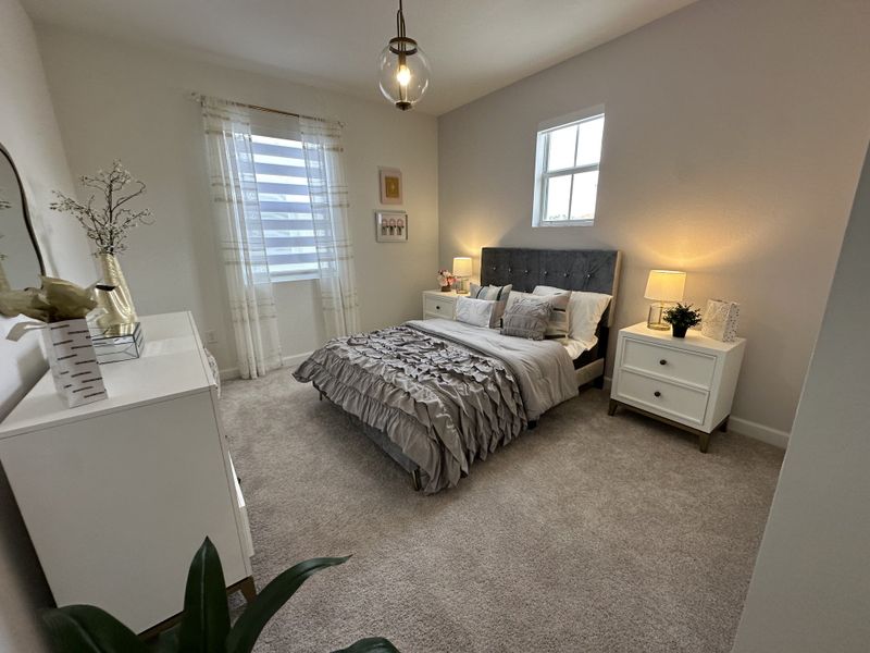 A cozy bedroom with plush carpeting, elegant bedding, modern lighting, and stylish white furniture.