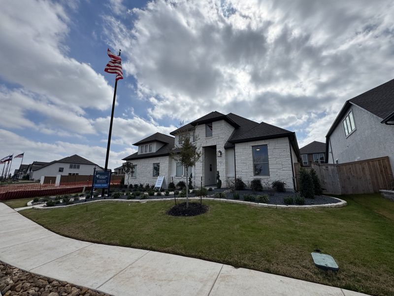 A modern stone exterior home with a manicured lawn, located in Mayfair 50' Homesites by Coventry Homes (New Braunfels, TX).