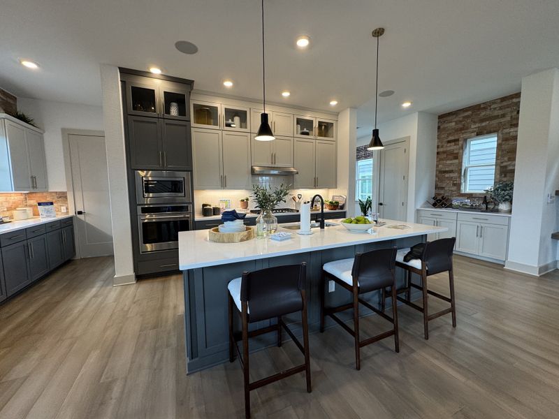 A modern kitchen with sleek gray cabinets, a central island, pendant lights, and hardwood floors.