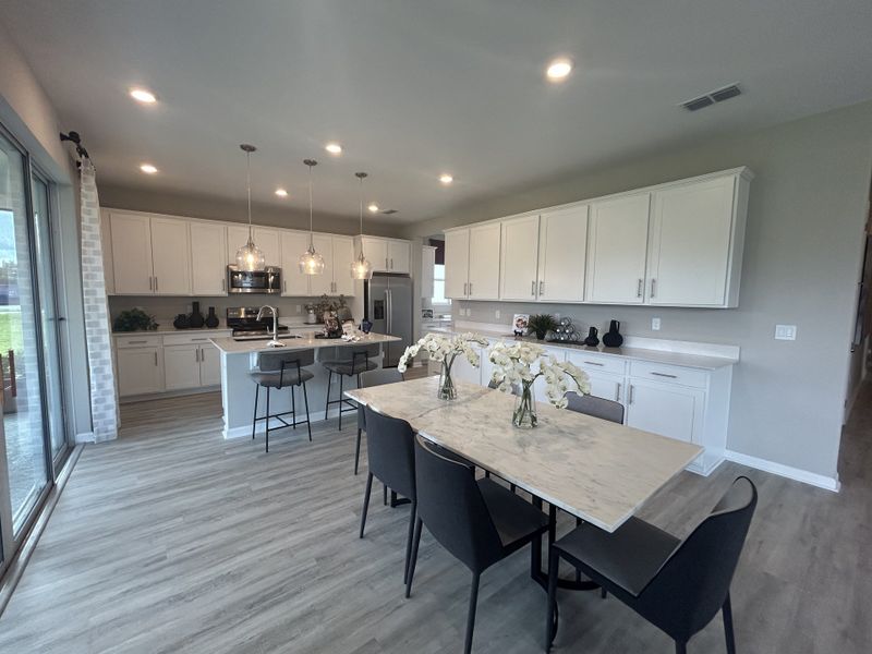 A modern kitchen with sleek white cabinetry, pendant lighting, and an elegant dining area with a large window view. A modern kitchen with sleek white cabinetry, pendant lighting, and an elegant dining area with a large window view.