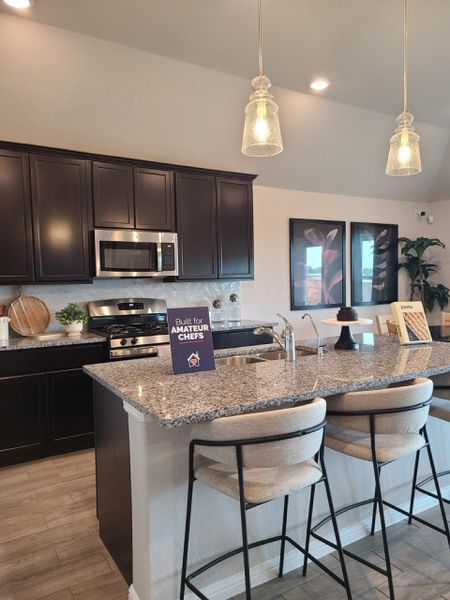 A modern kitchen with dark cabinetry, granite countertops, pendant lighting, and a cozy breakfast bar. A modern kitchen with dark cabinetry, granite countertops, pendant lighting, and a cozy breakfast bar.