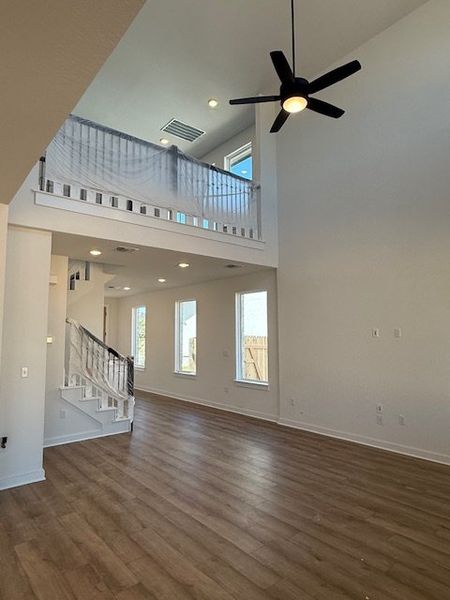 A spacious living area with high ceilings, wood floors, and a modern ceiling fan, featuring an upstairs balcony.