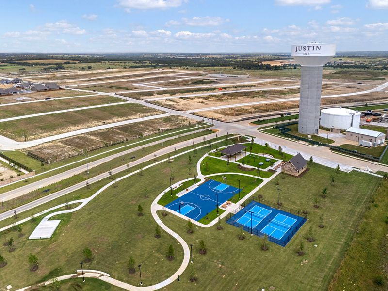 Aerial view of Justin, Texas community park with basketball and tennis courts, pavilion, and water tower near new development lots. Aerial view of Justin, Texas community park with basketball and tennis courts, pavilion, and water tower near new development lots.