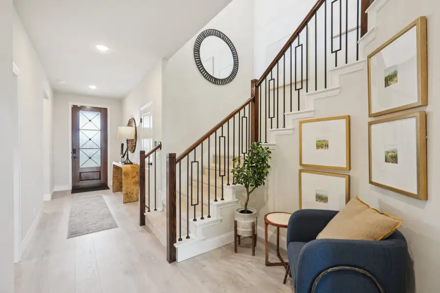 Entryway foyer with wood staircase, black iron balusters, light hardwood floors, and framed art on the wall Entryway foyer with wood staircase, black iron balusters, light hardwood floors, and framed art on the wall