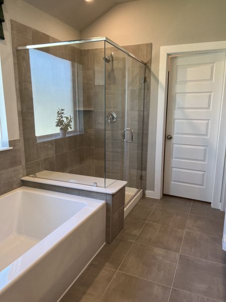 A modern bathroom with a glass shower, spacious bathtub, and neutral-toned tile flooring.