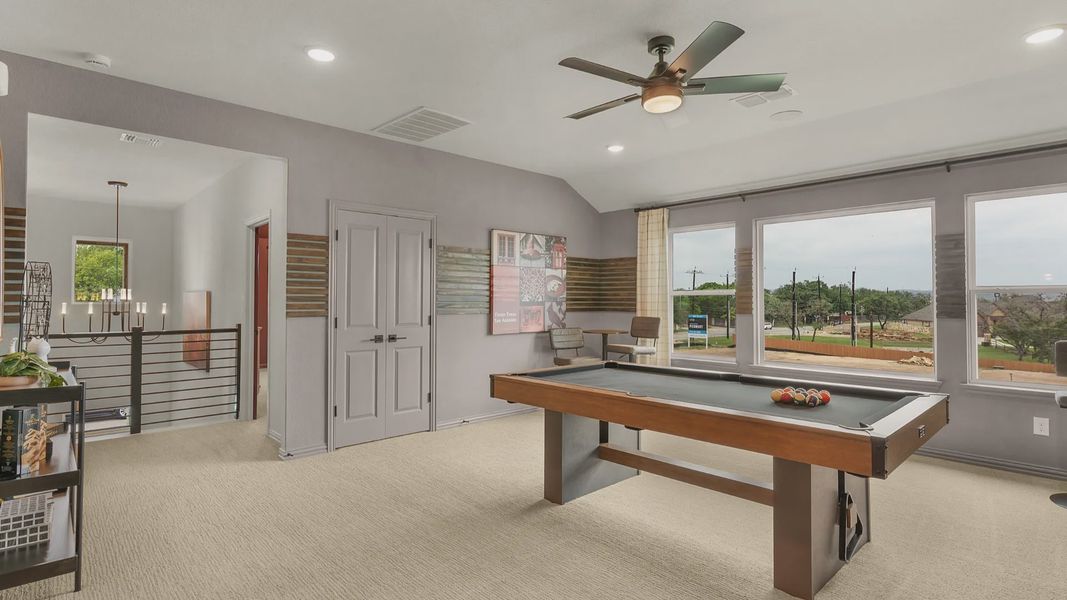Second-floor game room with large windows and a ceiling fan, connected to a dedicated media room for entertainment.