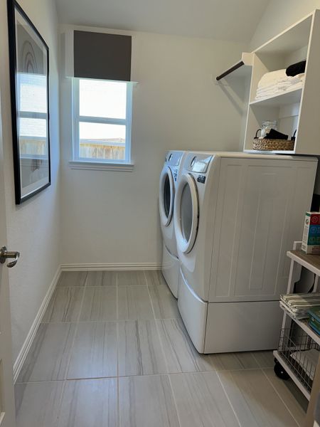 A sleek laundry room with gray tiled floors, modern appliances, shelving, and soft natural light. A sleek laundry room with gray tiled floors, modern appliances, shelving, and soft natural light.