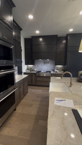 A sleek kitchen with dark cabinetry, marble countertops, stainless appliances, and a chic farmhouse sink.