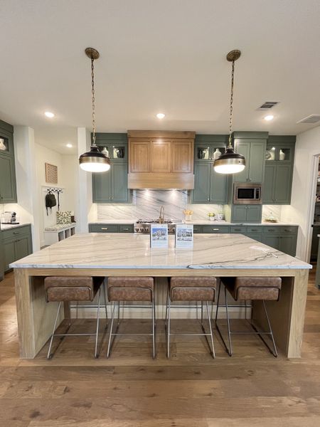 A modern kitchen featuring a large marble island, elegant pendant lights, and sleek green cabinetry.