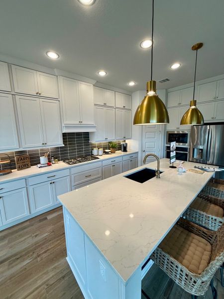 A sleek kitchen with white cabinetry, marble countertop island, brass accents, and modern lighting.