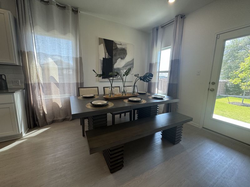 A sleek dining area features a modern table, benches, and artistic décor, flooded with natural light from large windows.
