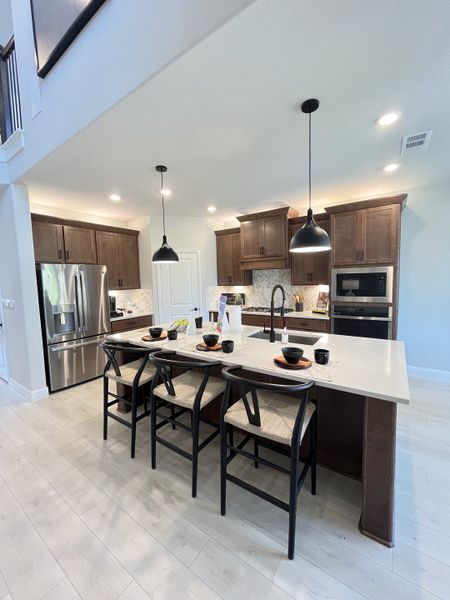 A modern kitchen featuring dark wood cabinets, sleek stainless appliances, and a spacious island with stylish pendant lighting.