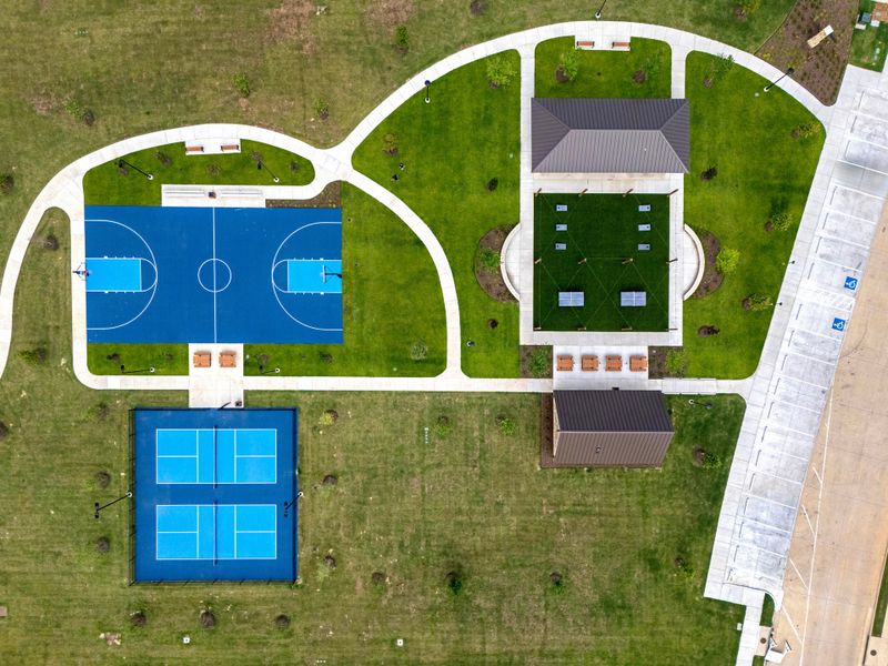 Bird's-eye view of residential community park with basketball court, pickleball courts, pavilion, and landscaped grounds Bird's-eye view of residential community park with basketball court, pickleball courts, pavilion, and landscaped grounds