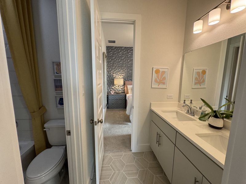 A modern bathroom with a dual sink vanity, geometric tiles, and cozy decor leading into a stylishly adorned bedroom.