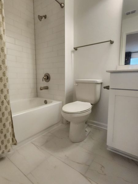 A cozy bathroom with a tiled shower-tub combo, sleek fixtures, and a modern white vanity.