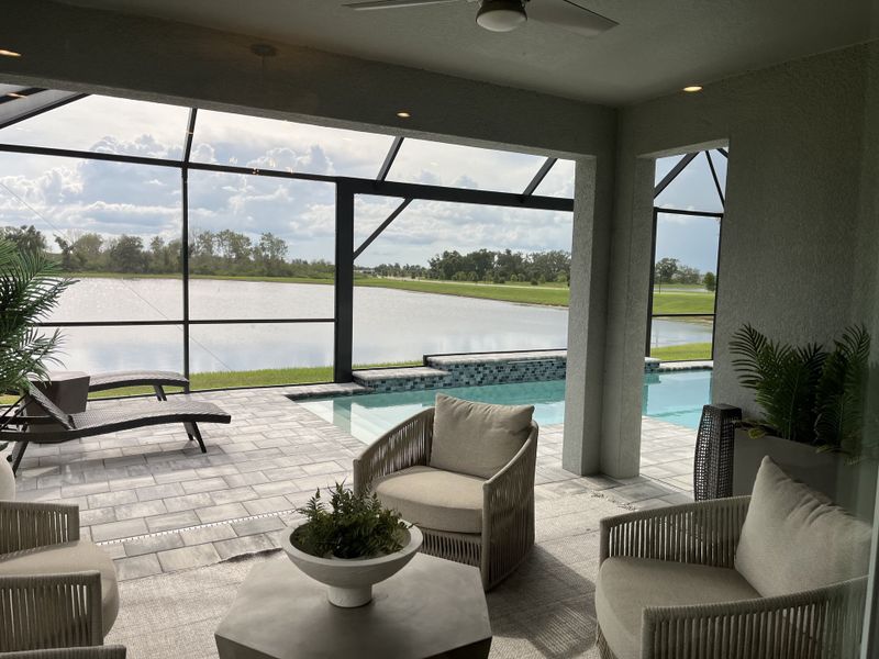 A serene patio with plush seating, overlooking a tranquil pool and scenic waterfront view, surrounded by lush greenery.