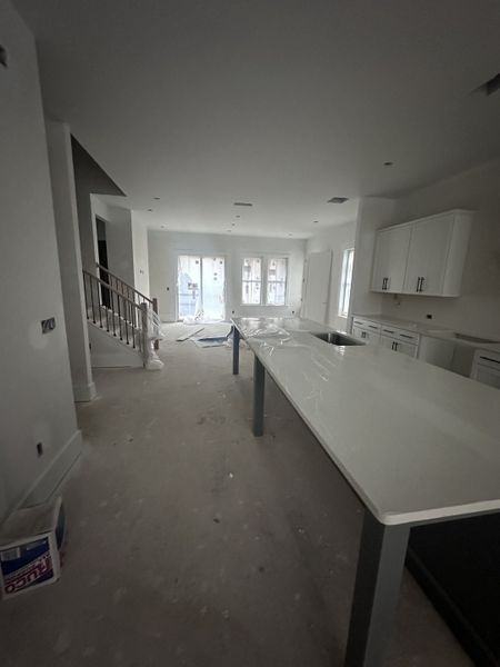 An expansive kitchen under construction with a large island, modern cabinets, and ample natural light.