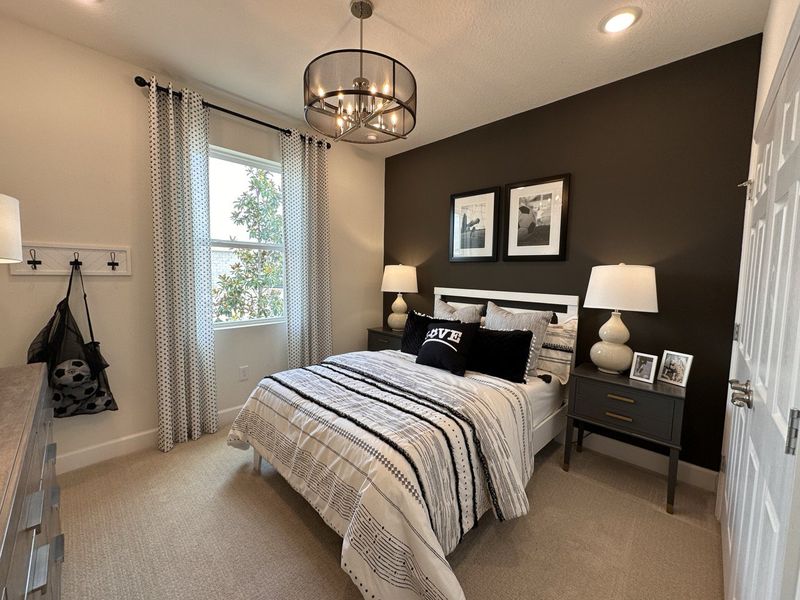 A cozy bedroom with a modern chandelier, striped bedding, and elegant decor featuring a dark accent wall.