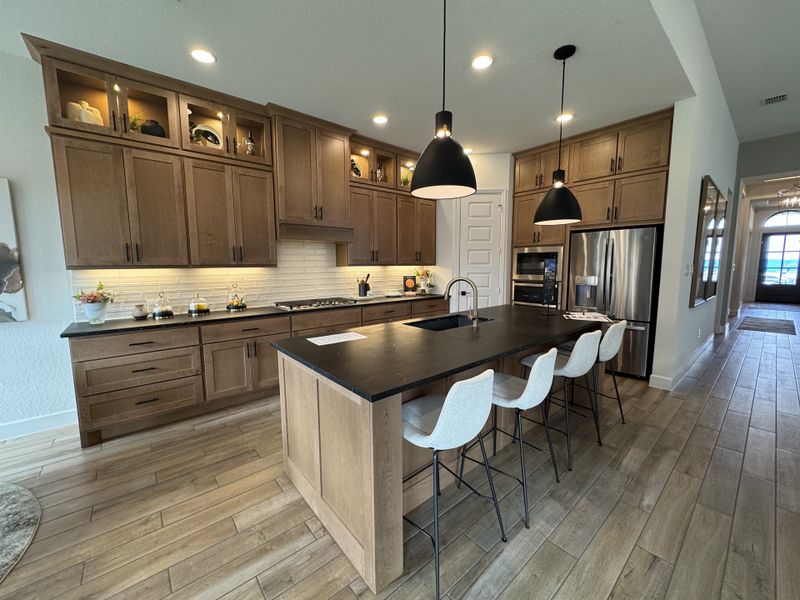 A modern kitchen featuring wooden cabinetry, a sleek island with pendant lighting, and stainless steel appliances.