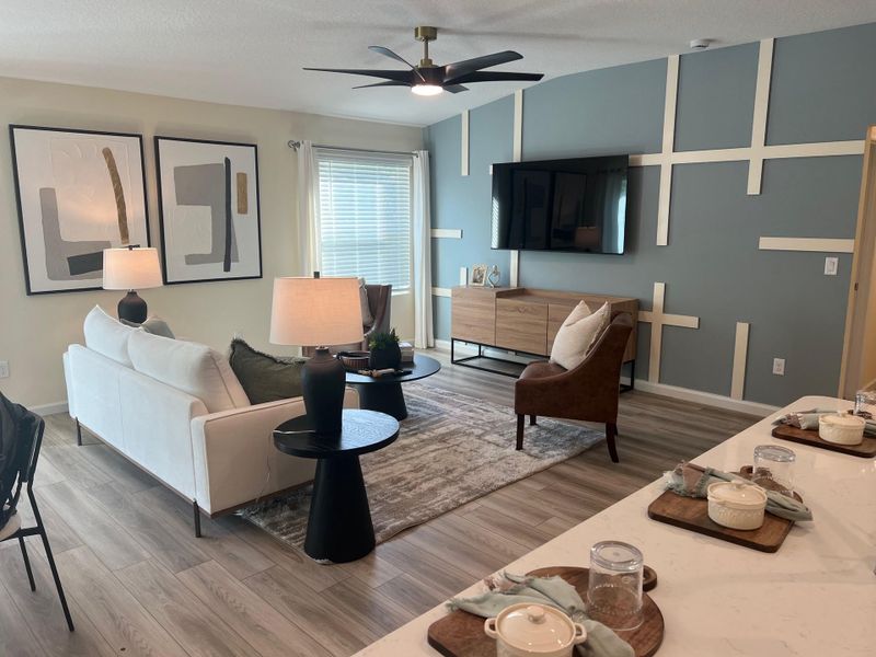 A modern living room with sleek décor, geometric wall art, elegant furniture, and a ceiling fan.
