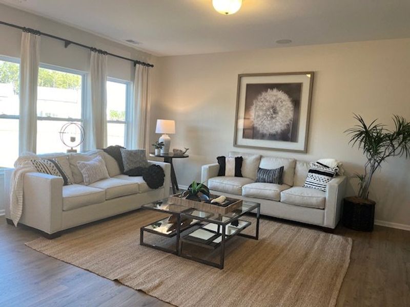 A cozy living room with neutral sofas, a glass coffee table, and elegant decor, featuring large windows and soft lighting.