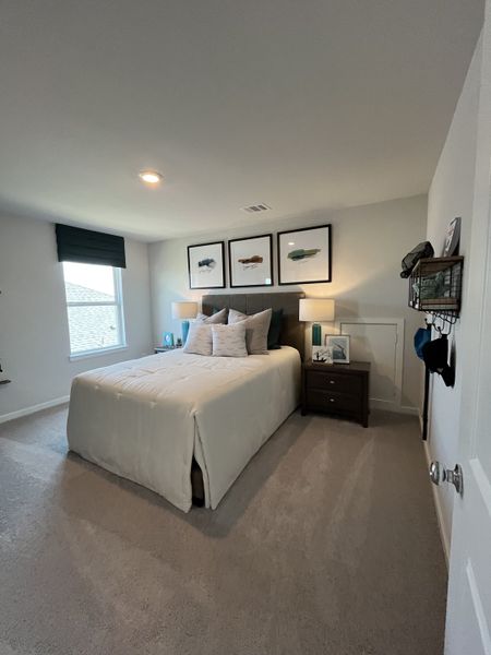 Cozy bedroom with a plush bed, modern decor, and ample natural light. Features framed artwork and elegant lighting.