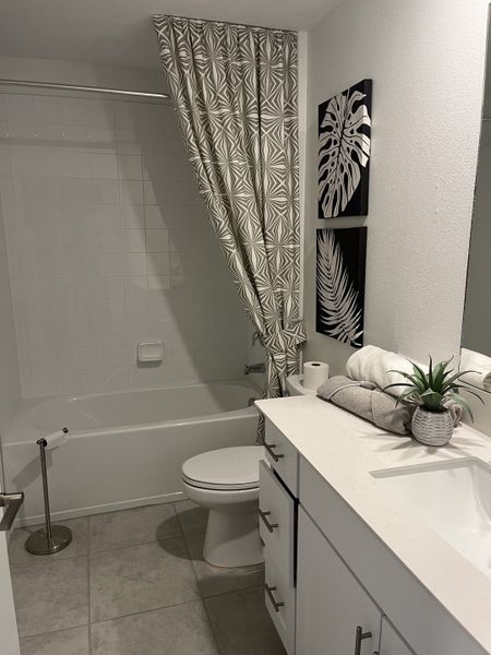 A modern bathroom with geometric shower curtain, white vanity, and tropical-themed decor. A modern bathroom with geometric shower curtain, white vanity, and tropical-themed decor.