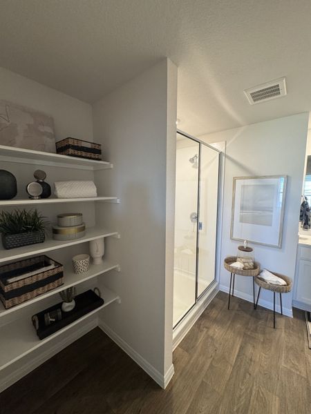 A modern bathroom with sleek shelving, a glass shower, and cozy wood floors.